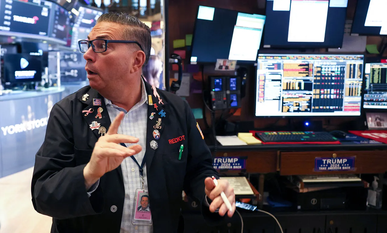 A trader works on the floor of the New York Stock Exchange at the opening bell in New York City, on April 7, 2025, standing near a workstation displaying “Trump 2024: Take America Back” bumperstickers