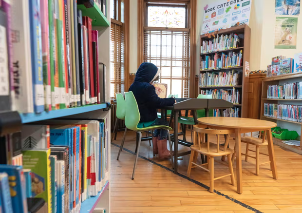 A young girl reads along the Canada-US international border line inside the Haskell Free Library and Opera House in Derby Line, Vermont, on 21 March 2025