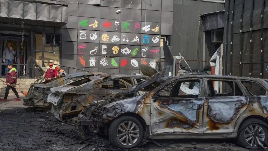 Municipal workers clean up near burnt cars in the residential area following Russia’s drone attack in Kyiv, Ukraine, Sunday, May 4, 2025