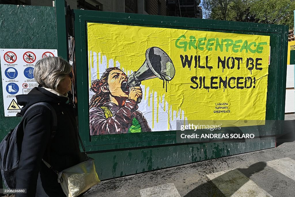 A woman walks past a banner by Italian street artist Laika in support of Greenpeace pasted in front of the US Embassy in Rome following a recent US court ruling that found the environmental group liable for hundreds of millions of dollars of damages, on April 9, 2025. On March 19, a court in North Dakota ordered Greenpeace to pay over $660 million to an oil pipeline company, a decision widely seen as a chilling attack on climate activism worldwide. Environmental defenders have rallied behind Greenpeace after the shock verdict, raising concerns that courtrooms are increasingly being used to silence critics of the fossil fuel industry. (Photo by ANDREAS SOLARO / AFP) (Photo by ANDREAS SOLARO/AFP via Getty Images)