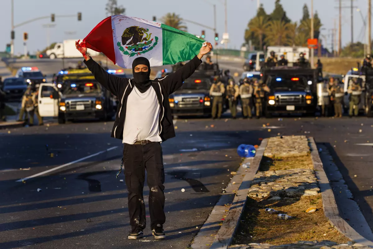 A protester carries a Mexican flag as L.A. County sheriff’s deputies form a law enforcement line. (Gina Ferazzi/Los Angeles Times)