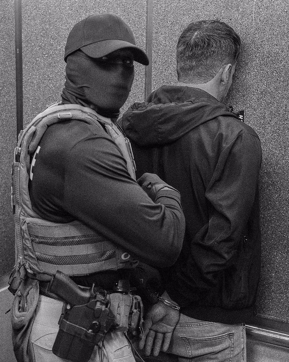 a black and white photo of a masked ICE agent detaining a man in immigration court. Olga Fedorova / AP