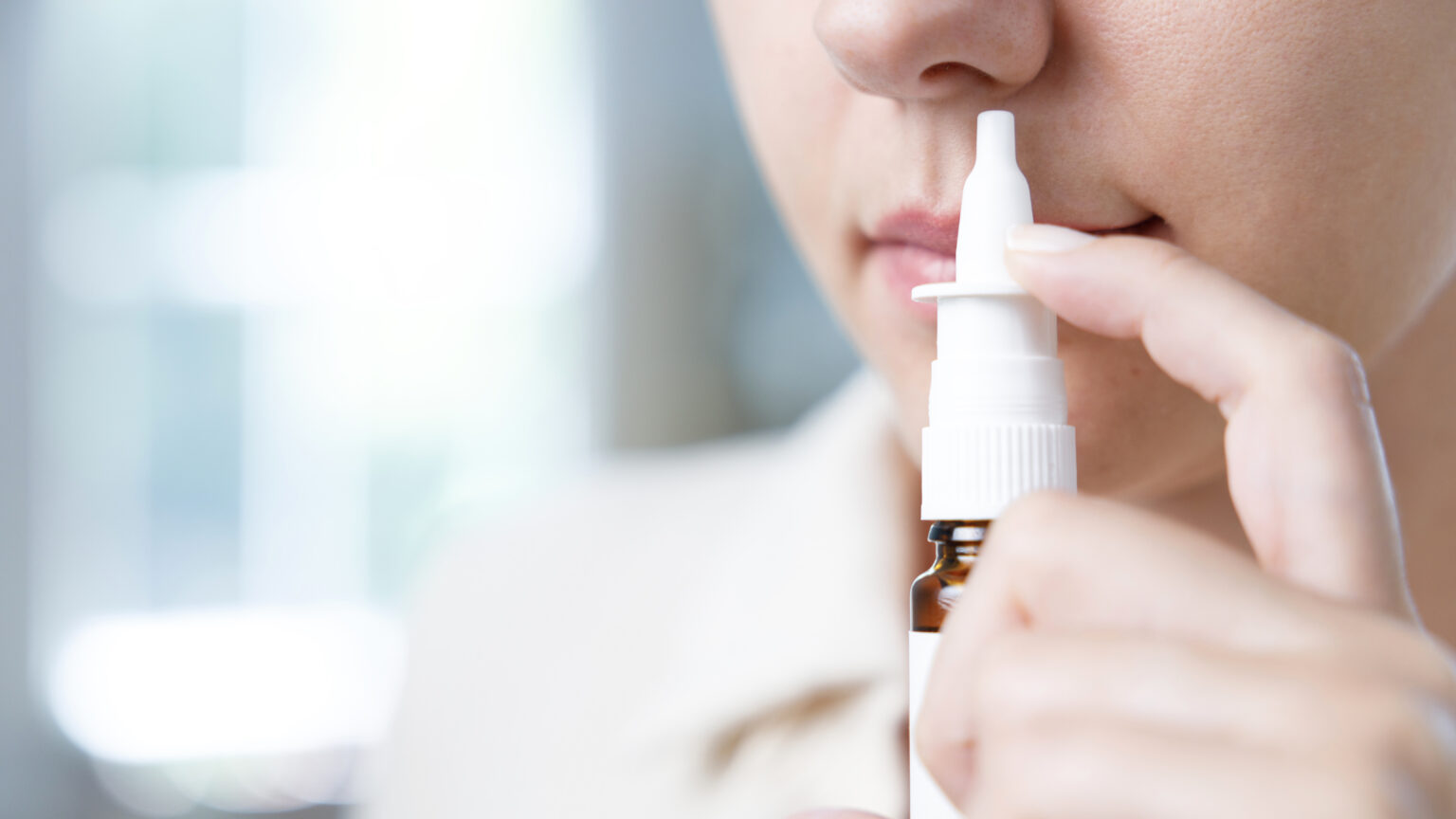 Close-up shot of sick young woman using nasal spray