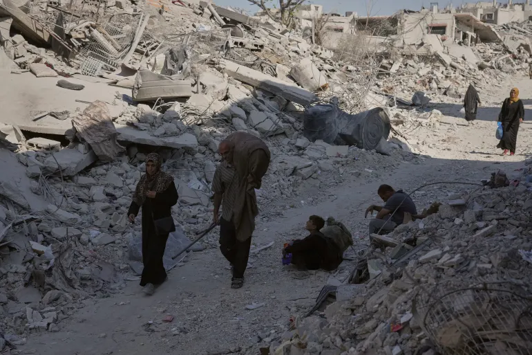 Palestinians walk among destroyed buildings in Gaza City, on Thursday, October 16, 2025 [Jehad Alshrafi/AP]