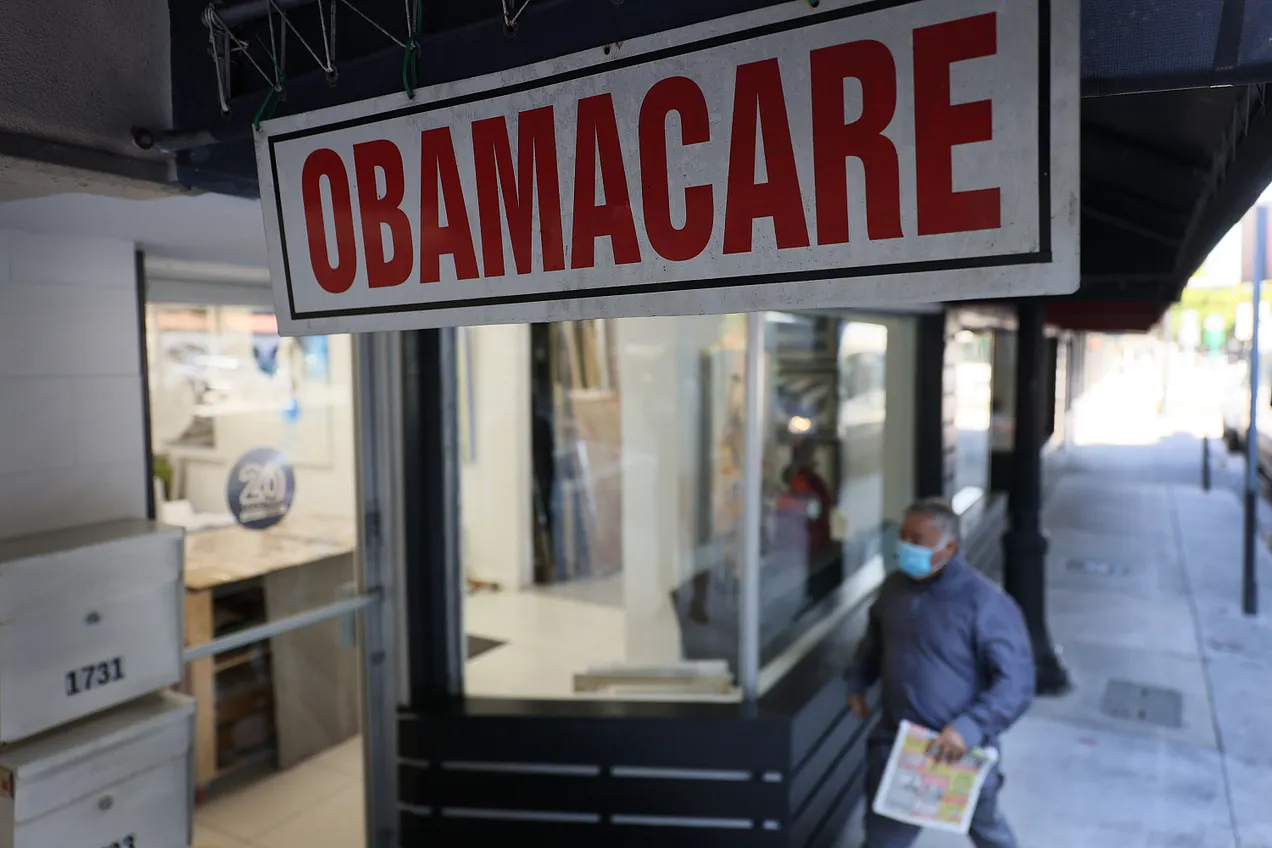 A pedestrian walks past the Leading Insurance Agency, which offers plans under the Affordable Care Act (Obamacare) on January 28, 2021 in Miami, Florida. (Photo by Joe Raedle/Getty Images)