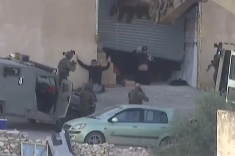image grab obtained from Palestine TV footage on November 28, 2025, and filmed a day earlier, shows two Palestinian men raising their hands in surrender before Israeli forces, moments before being shot by soldiers during a military operation in the Israeli-occupied West Bank city of Jenin [AFP]