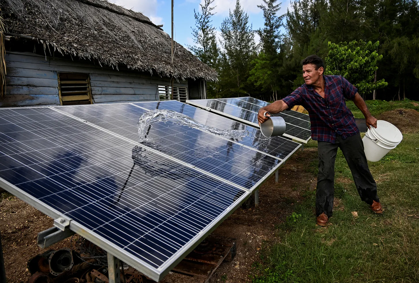 A Cuban farmer cleans the solar panels outside his modest home