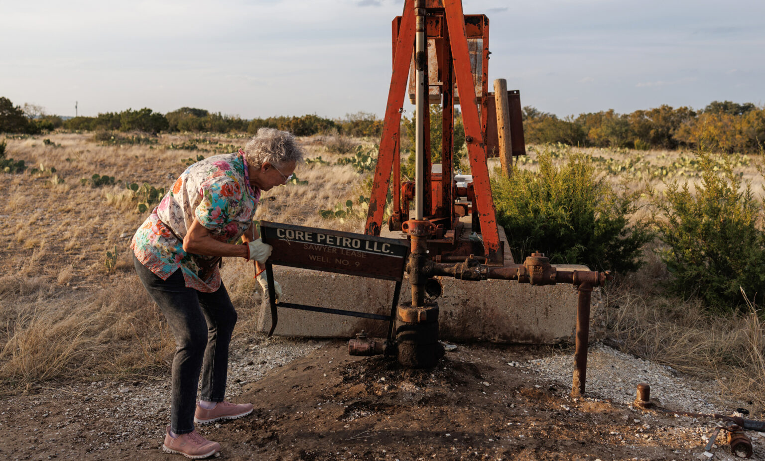 Jackie Chesnutt props up a sign next to a leaking oil well operated by CORE Petro on her property near Knickerbocker, Texas, on Nov. 18, 2025.