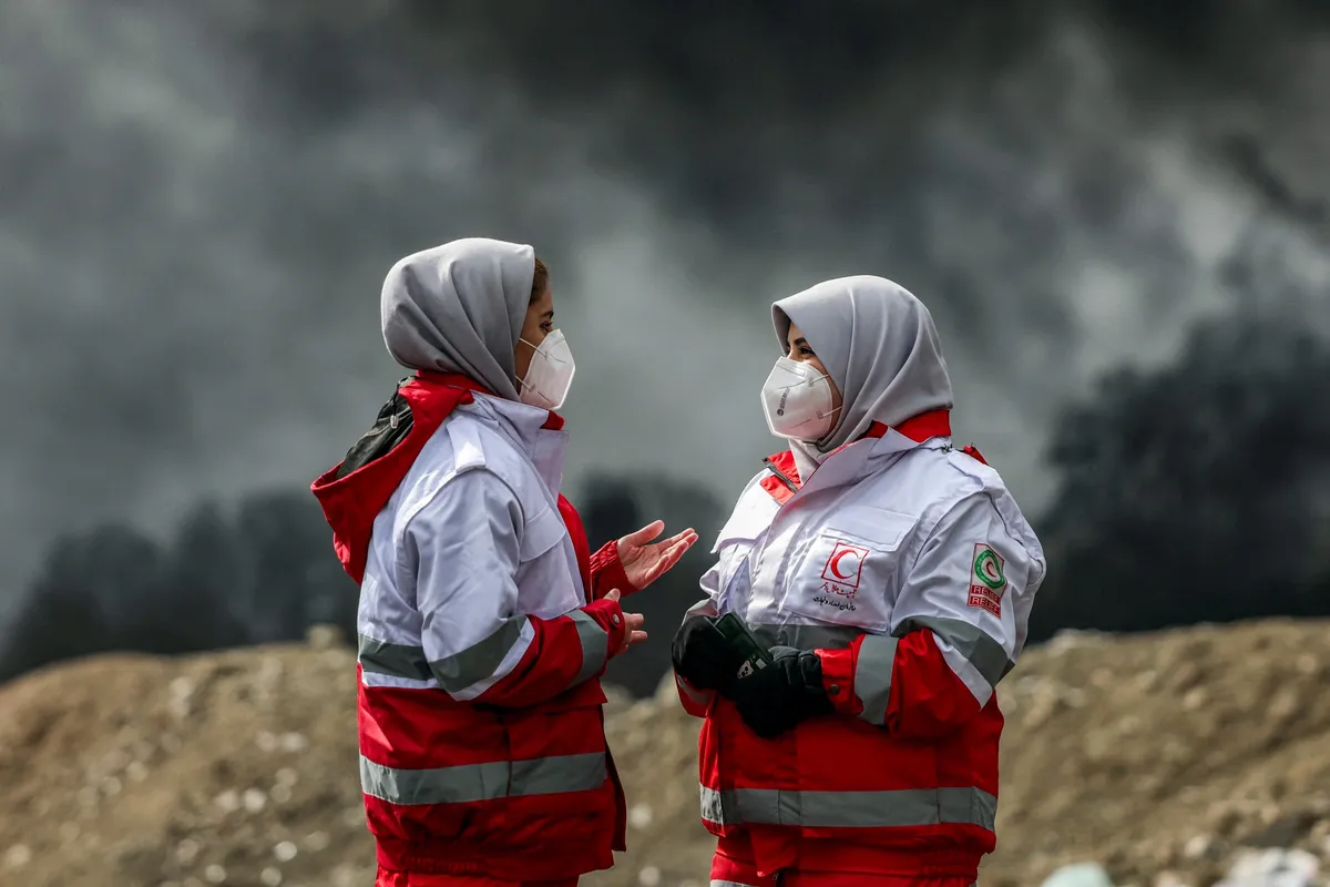 Iranian Red Crescent workers near smoke from an overnight airstrike on an oil refinery in northwestern Tehran, on March 8.Source: AFP/Getty Images