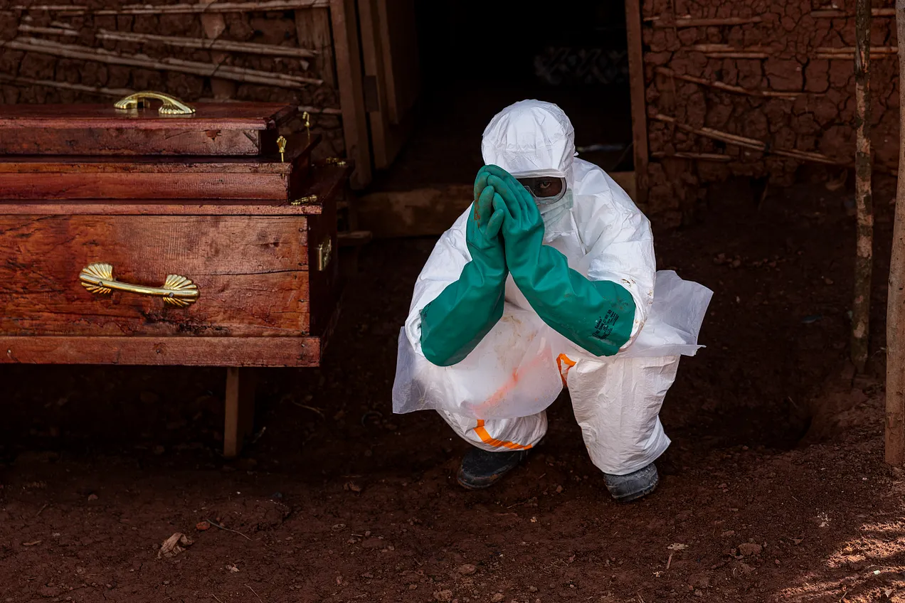 A health worker wearing protective equipment crouches beside the coffin of a suspected Ebola victim during safe burial procedures outside a family home in the community of Mongbwaluon on May 24, 2026 in the Democratic Republic of Congo. (Photo by Michel Lunanga/Getty Images)