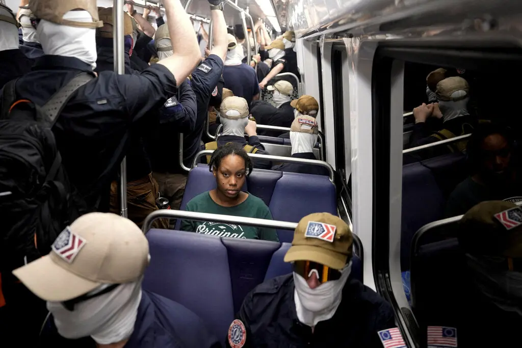 A commuter sits as members of the group Patriot Front ride the metro on the Fourth of July in Washington, D.C.Credit...Cheney Orr/Reuters