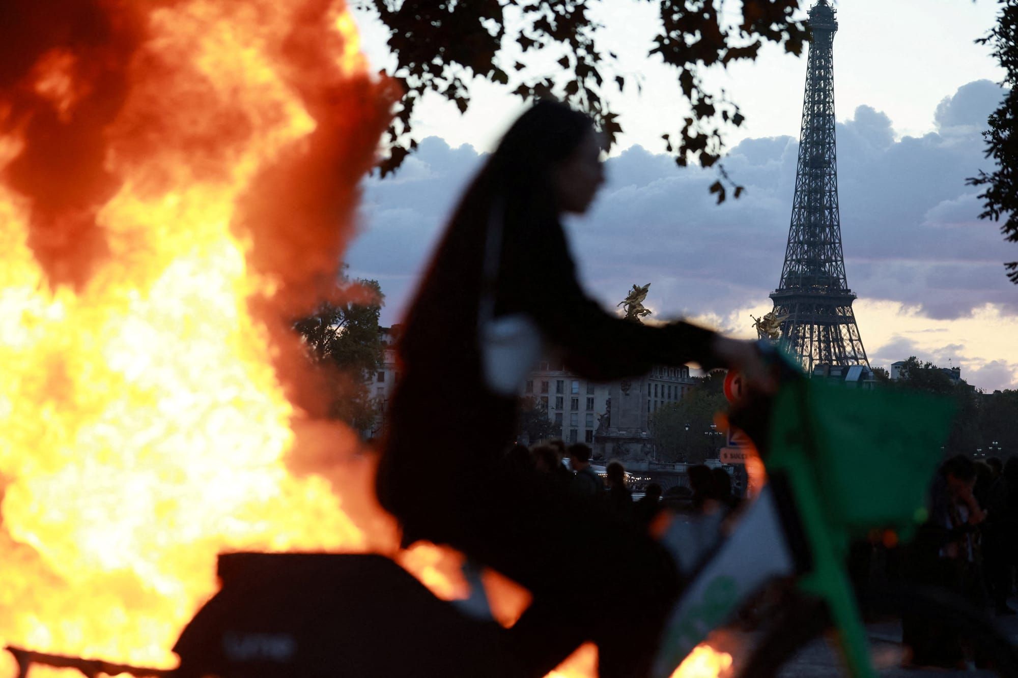 A woman rides a bicycle past a burning barricade near the Tuileries Garden with the Eiffel Tower in the background | REUTERS/Stephanie Lecocq/File Photo