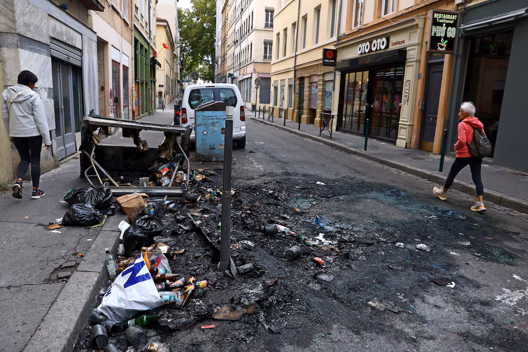 People walk past burnt debris on the side of a street, the day after clashes during a second day of nationwide protests against the cost of living and rising fuel prices, in Lyon, France, October 25, 2026. REUTERS/Lisi Niesner